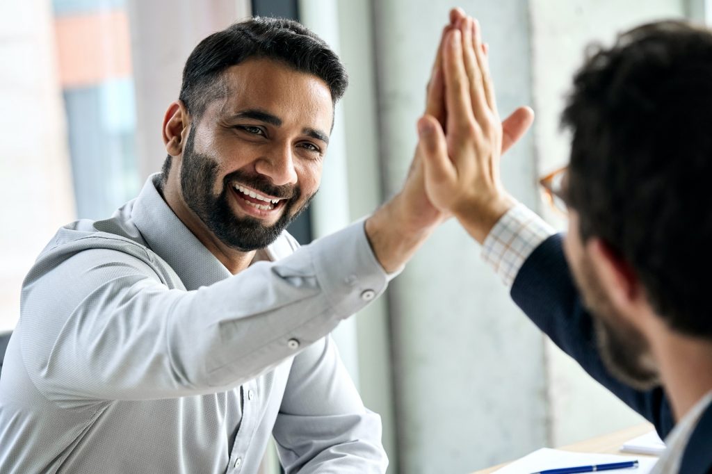 Two happy international businessmen giving high five at meeting board room.